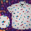 Load image into Gallery viewer, Full view of the 7-Strong Block Party youth button down, featuring various colored blocks of different arrangements inspired by a classic video game, cascading down the shirt against a grayish background featuring shadows of the same shapes. The shirt is presented on a background of similar design.In the bottom left is a detail circle with a close up of the design.
