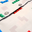 Load image into Gallery viewer, Close up of the middle button portion of the Block Party shirt detailing the various colored blocks of different arrangements inspired by a classic video game, cascading down the shirt against a grayish background featuring shadows of the same shapes. The shirt is presented on a background of similar design.
