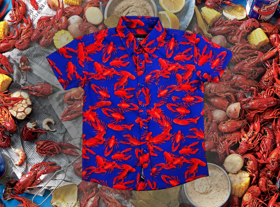 Full view of the 7-Strong Dat Boil shirt in deep navy blue with red crawfish patterned throughout overlapping one another. The shirt itself sits on a background image of items from a Crawfish Boil such as crawfish, seasoning, corn, and potatoes. 