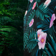 Load image into Gallery viewer, Side mid drift button view of the Youth 7-Strong &quot;Tropic Like It&#39;s Hot&quot; button down shirt - a black shirt with distinctive green palm trees and pink, white, and purple flowers peering out from behind the palms. Shirt is shown on a tropical rainforest background.
