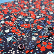 Load image into Gallery viewer, Middle button region view of the youth 7-Strong &quot;Aye Poppy&quot; button down, featuring an array of red poppys with white sprigs on a deep navy blue shirt. The shirt is displayed against a partly cloudy sky. 
