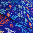 Load image into Gallery viewer, Mid torso view of the 7-Strong &quot;Coral of the Story&quot; youth button down shirt. Color of the shirt is blue with vibrant purple, teal, orange sea life imagery - particularly fish and coral reef. 
