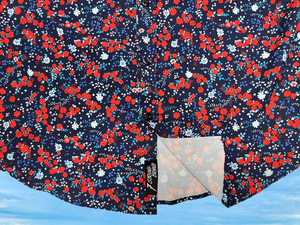 Bottom half sweep tag view of the youth 7-Strong "Aye Poppy" button down, featuring an array of red poppys with white sprigs on a deep navy blue shirt. The shirt is displayed against a partly cloudy sky. 