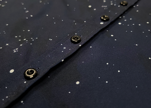 Midsection  view of the youth short-sleeve Stargazer button down shirt. A deep navy blue shirt with constellation star patterns throughout. The shirt is displayed against a night sky full of stars.