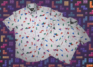 Full view of the 7-Strong Block Party adult and youth button downs overlapping each other, featuring various colored blocks of different arrangements inspired by a classic video game, cascading down the shirt against a grayish background featuring shadows of the same shapes. The shirt is presented on a background of similar design.
