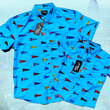 Load image into Gallery viewer, Full view of overlapping adult and youth 7-Strong &quot;Pennant to Win It&quot; shirt, which is sky blue with texture, featuring various triangular flags featuring baseball&#39;s prominent cities patterned throughout. The shirt is featured against abackground is sunset at a major league stadium. 
