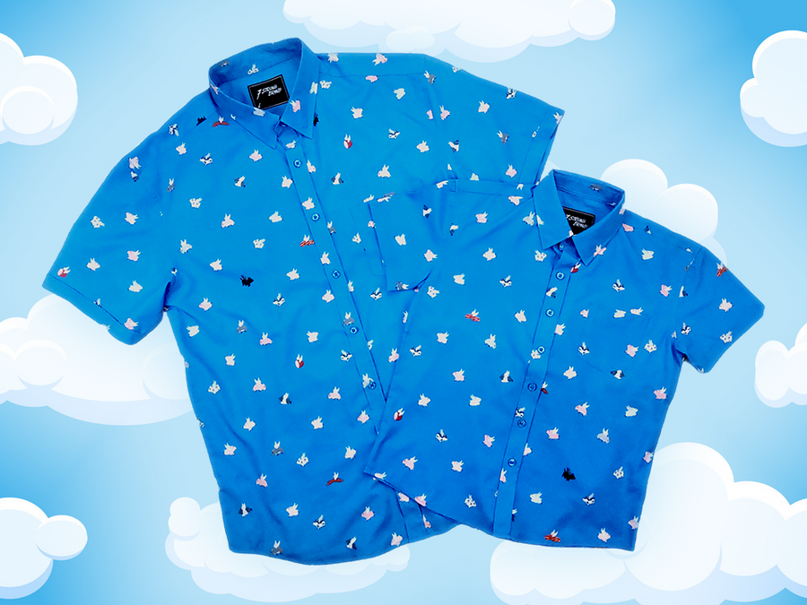 Full shot of the adult and youth 7-Strong "When Pigs Fly" shirt, showcasing various pigs and meats flying against a blue, muted cloud background. Shirt is displayed against a background of cartoon clouds.
