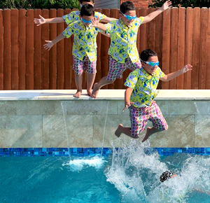 Youth model wearing the 7-Strong "Late Bloomer" youth button down - a yellow background shirt with white and blue flowers patterned all over it. Model is being shown multiple times in edited phases of jumping into a pool with the shirt on and googles... from beginning to jumping in to splashing into the pool. 