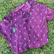 Load image into Gallery viewer, Full view of the Cup of Life adult and youth button ups, overlapping one another, a off-maroon colored shirt decorated throughout with falling gold confetti and depictions of the World Cup statue. The shirt is laid out on a grass pitch. 
