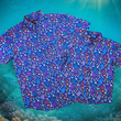 Load image into Gallery viewer, Full view shot of the 7-Strong &quot;Coral of the Story&quot; youth and adult button down shirts overlapping one another. Color of the shirt is blue with vibrant purple, teal, orange sea life imagery - particularly fish and coral reef. The shirt is shown against an underwater background showcasing coral.
