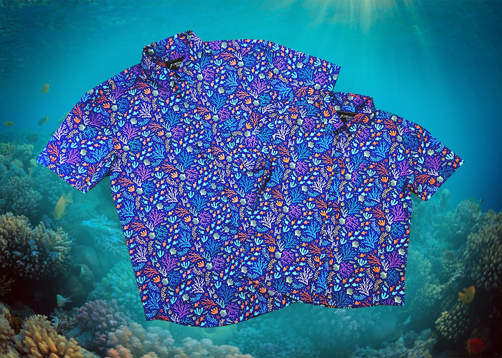 Full view shot of the 7-Strong "Coral of the Story" youth and adult button down shirts overlapping one another. Color of the shirt is blue with vibrant purple, teal, orange sea life imagery - particularly fish and coral reef. The shirt is shown against an underwater background showcasing coral.