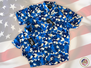 Full view close up of the 7-Strong "Service Stars" adult and youth button-ups overlapping each other, featuring blue and creme colored camouflage with white weathered stars throughout. The shirt is featured against a waving U.S. Flag faded into the background. Bottom right is the 22 Flag Co logo.