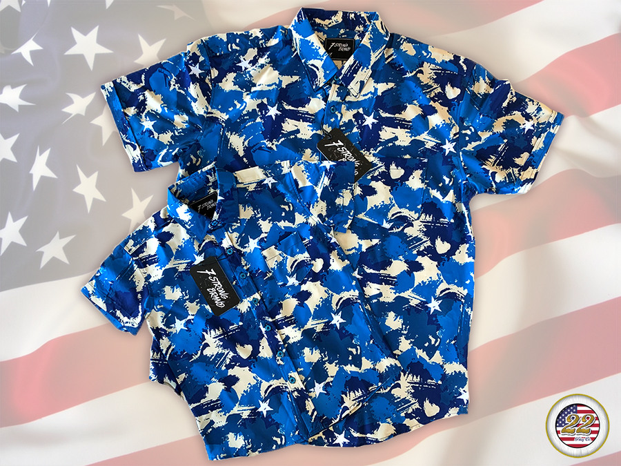 Full view close up of the 7-Strong "Service Stars" adult and youth button-ups overlapping each other, featuring blue and creme colored camouflage with white weathered stars throughout. The shirt is featured against a waving U.S. Flag faded into the background. Bottom right is the 22 Flag Co logo.