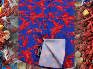 Close-up sweep tag view of the 7-Strong Dat Boil shirt in deep navy blue with red crawfish patterned throughout overlapping one another. The shirt itself sits on a background image of items from a Crawfish Boil such as crawfish, seasoning, corn, and potatoes. 