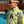 Load image into Gallery viewer, Youth model wearing the 7-Strong &quot;Late Bloomer&quot; youth button down - a yellow background shirt with white and blue flowers patterned all over it. Model is standing by the pool in sunglasses with the shirt being shown at a medium close up on the body. 
