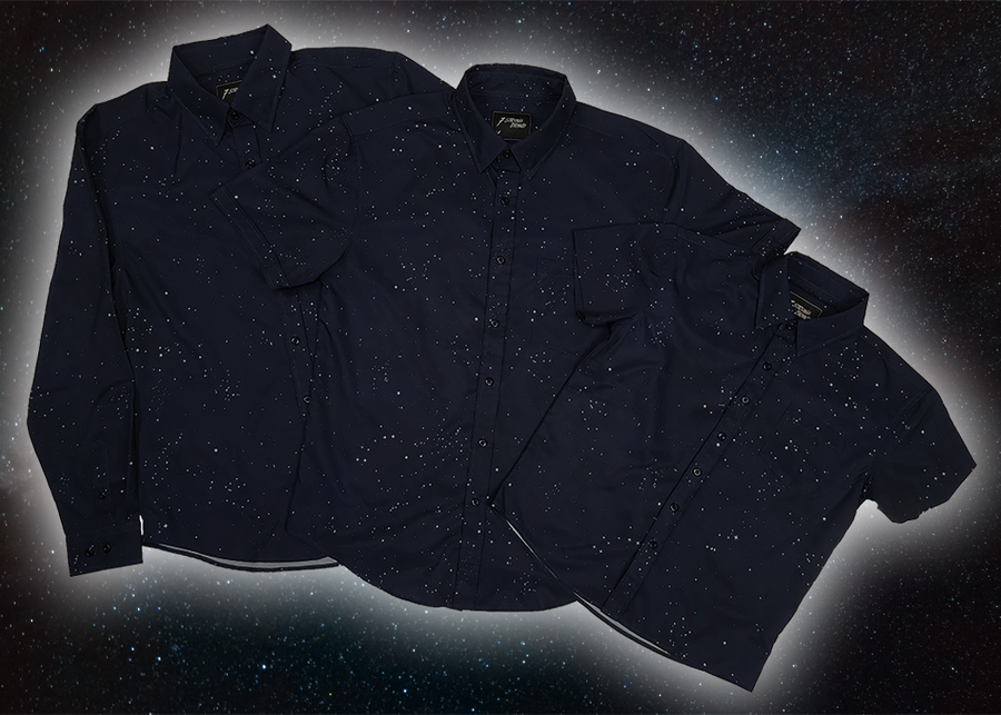 Full view of the long-sleeve, and short-sleeve adult and youth Stargazer button down shirts overlapping one another. A deep navy blue shirt with constellation star patterns throughout. The shirt is displayed against a night sky full of stars.