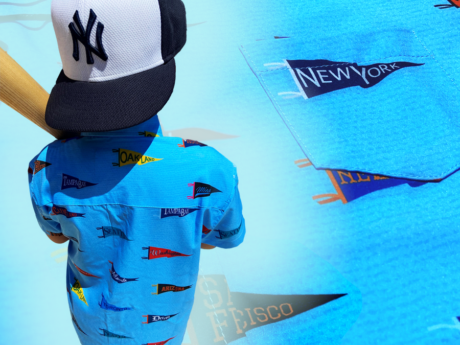 Back midsection view of a youth male model, yielding baseball bat, wearing a NY Yankees hat sporting the 7-Strong "Pennant to Win It" shirt, which is sky blue with texture, featuring various triangular flags featuring baseball's prominent cities patterned throughout. The shirt is featured against a background is a backdrop of the Pennants featured on the shirt.