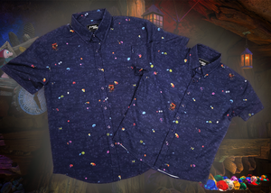 Full view shot of the 7-Strong "Mine Train" adult and youth button ups overlapping one another. Shirt is a deep purple with a rock quarry depicting ghosted design showcasing various colors of gemstones and mine train carts throughout. The shirt itself is displayed against a background of a mine shaft and various gems found in buckets. 
