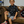 Load image into Gallery viewer, Male youth modeling the youth short sleeve version of &quot;Got &#39;Em!&quot; The button down features various athletic fashion sneakers in an 8-bit format arranged all over a black shirt.  Child is sitting on a coach looking at camera, while on the right is detail circle showcasing various shoes designed on the shirt. 
