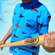 Load image into Gallery viewer, Midsection view of a youth male model, yielding baseball bat, sporting the 7-Strong &quot;Pennant to Win It&quot; shirt, which is sky blue with texture, featuring various triangular flags featuring baseball&#39;s prominent cities patterned throughout. The shirt is featured against a background is a backdrop of the Pennants featured on the shirt. 
