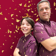 Load image into Gallery viewer, Male models, standing back-to-back, sporting the Cup of Life adult and youth button up, a off-maroon colored shirt decorated throughout with falling gold confetti and depictions of the World Cup statue. The models are standing against a confetti background that matches the shirt design.

