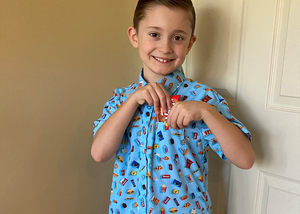Child model wearing the 7-Strong "Cheat Day" youth button down featuring various snacks, treats, and fast food features on a light blue shirt hiding candy in the shirt pocket.